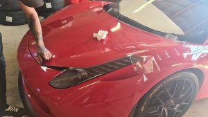 Pose d'un film de protection transparent sur le capot d'une Ferrari rouge.
