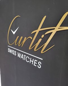 Logo en relief Curtit Swiss Watches, lettrage doré sur panneau noir pour une enseigne de luxe.