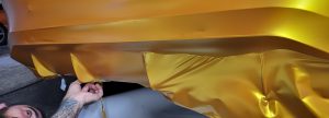 Pose d'un film de covering doré satiné sur un pare-choc de voiture par un expert.