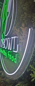 Enseigne lumineuse O BOWL Healthy Food avec lettrage néon sur un mur végétal.