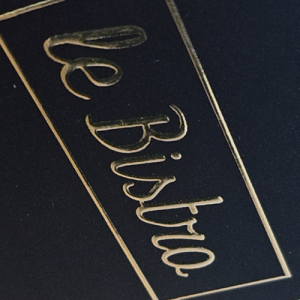 Logo "Le Bistro" avec une finition en dorure à chaud dorée sur un support noir texturé.